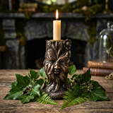 Bronze candle holder with a lit candle on a wooden surface with greenery