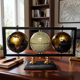 Three globe models on a stand in a room with books and a clock.