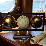 Three globe set on a stand with a magnifying glass and rolled map on a wooden surface.