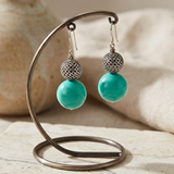 Pair of earrings with turquoise beads on a decorative stand.