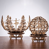 Two ornate laser-cut wooden decorative sculptures displayed on a wooden table against a light gray background. One sculpture features a central ballerina figure with coral-like branches, and the other is a circular tree-of-life design with dancers inside.