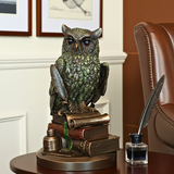 Decorative owl statue with books and inkwell on a table, with a chair and framed pictures in the background.