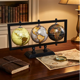 Three globe set on a stand with a magnifying glass and map on a wooden surface.