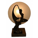 An Art Deco style table lamp featuring a bronze-colored dancing lady figure, with a frosted round glass panel behind it.
