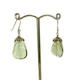 A pair of sterling silver earrings with green amethyst centers and additional silver petals, displayed on a stand.